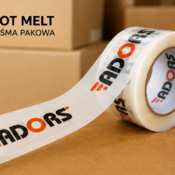 Taśma pakowa z nadrukiem ADORS na tle kartonów. Taśma z klejem Hot Melt przeznaczona do zaklejania paczek i przesyłek.